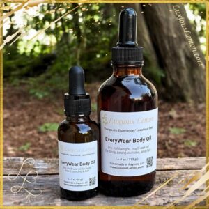 Glass bottle of Luxious Lemon Everywear Body Oil with golden-hued oil, surrounded by fresh citrus slices and glowing skin-care ambiance – 4 oz size and 1 oz size